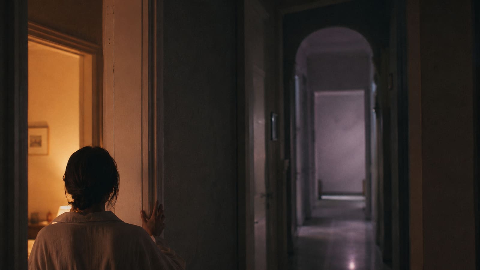 A figure at the threshold of a doorway at dawn, warm light behind, cool shadow ahead